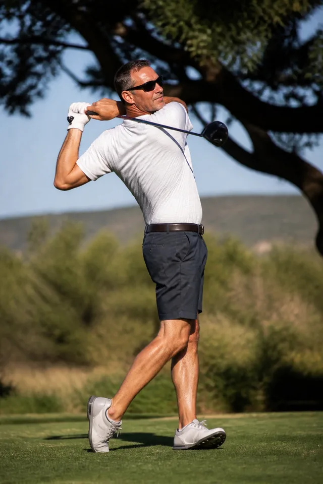 A man in dark polarized sunglasses finishing his swing on a sunny fairway